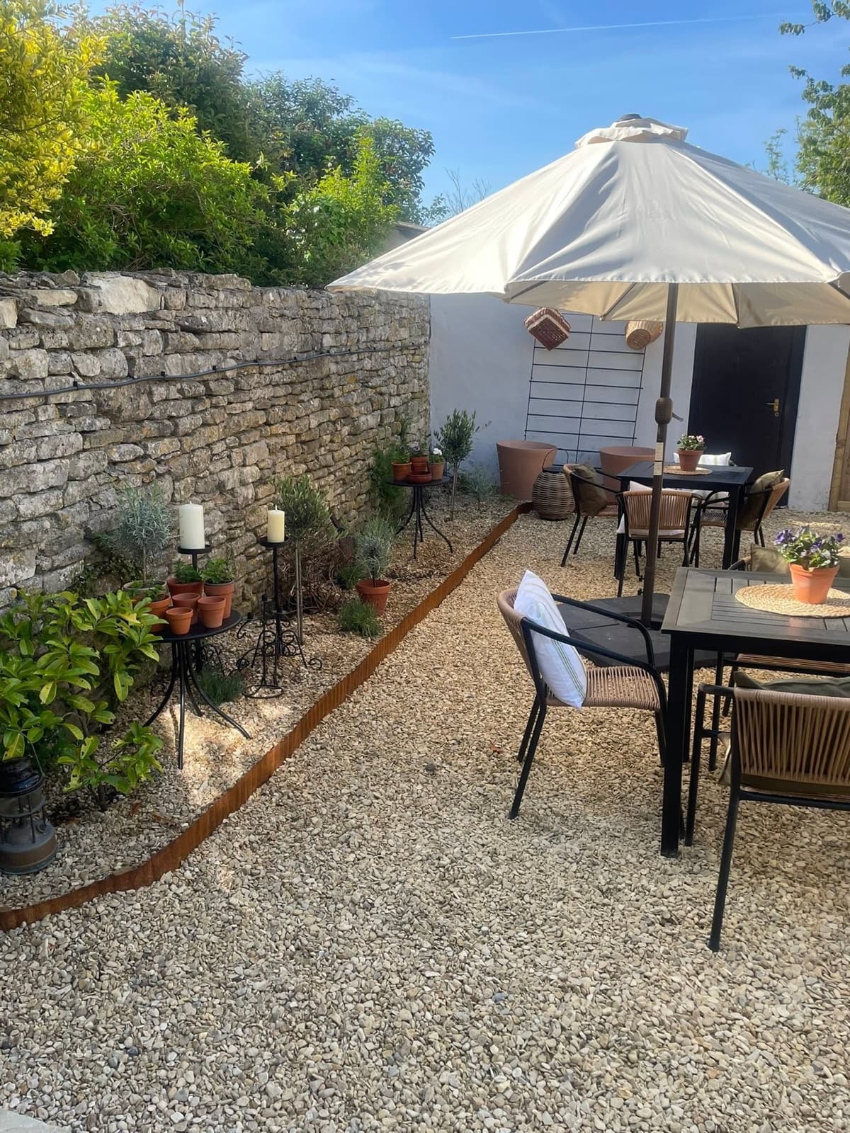 The courtyard garden at The Olive Tree — gravel, olive trees and tables under a parasol against the Cotswold stone wall